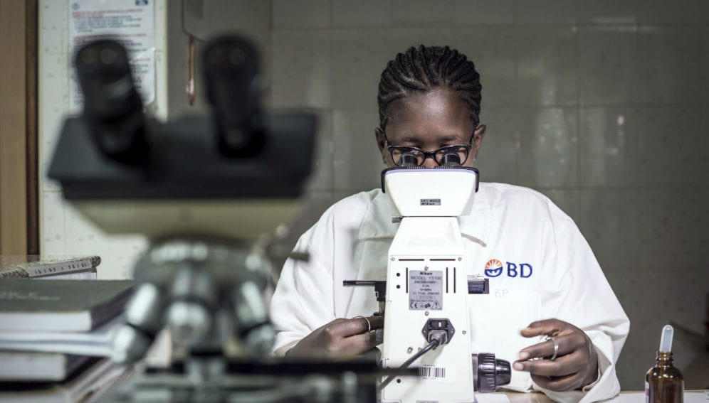 A woman examines a blood slide sample while testing for malaria