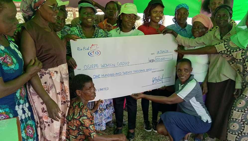 Women fish farmers with a dummy cheque given to them by Rio Fish limited for some of the fish they harvested.
