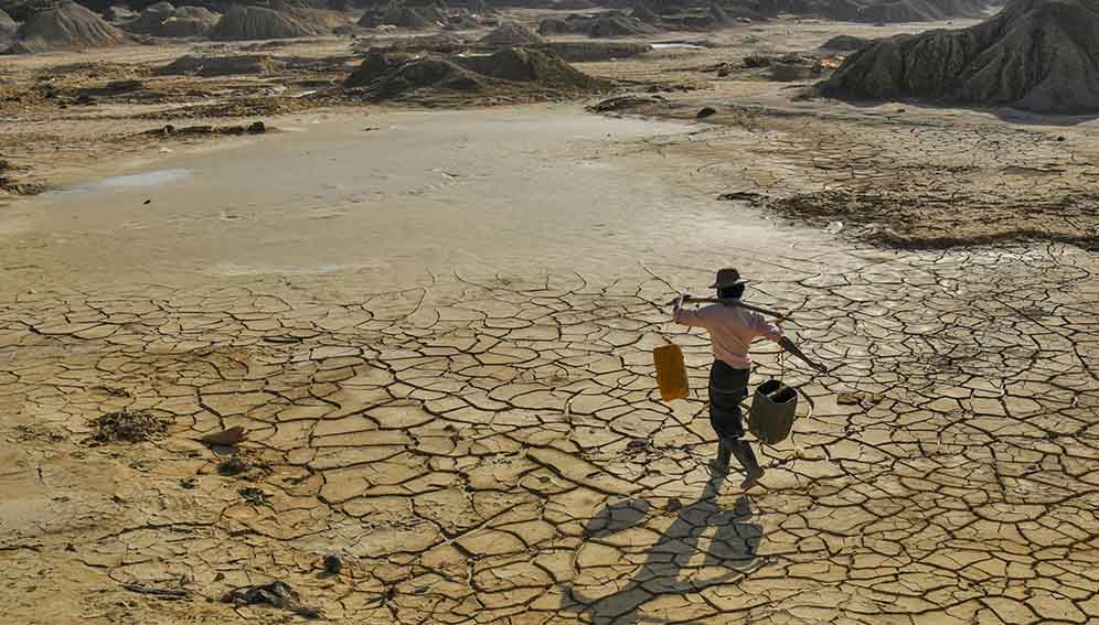 Man carrying water on cracked dry land in Myanmar. Photo by Pyae Phyo Aung