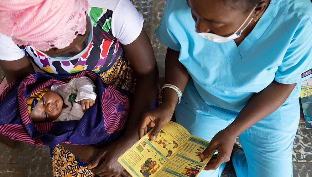 af_babyNmom_MAIN A nurse shares educational materials with mother to protect her family from malaria at Petifu Junction Health Centre in Sierra Leone on 9, August 2021.